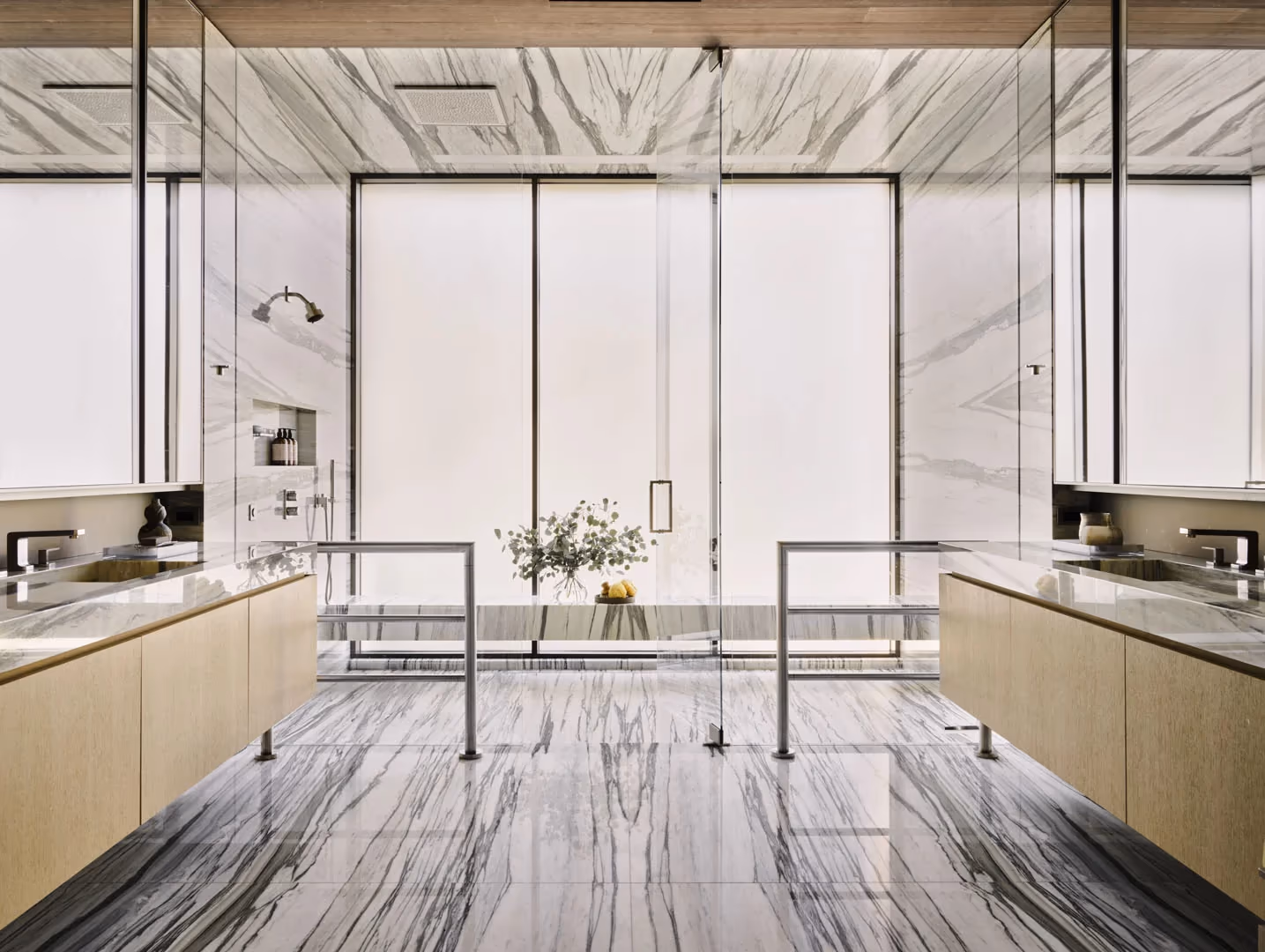 Bathroom with veined marble walls and floor, twin vanities and a glass shower
