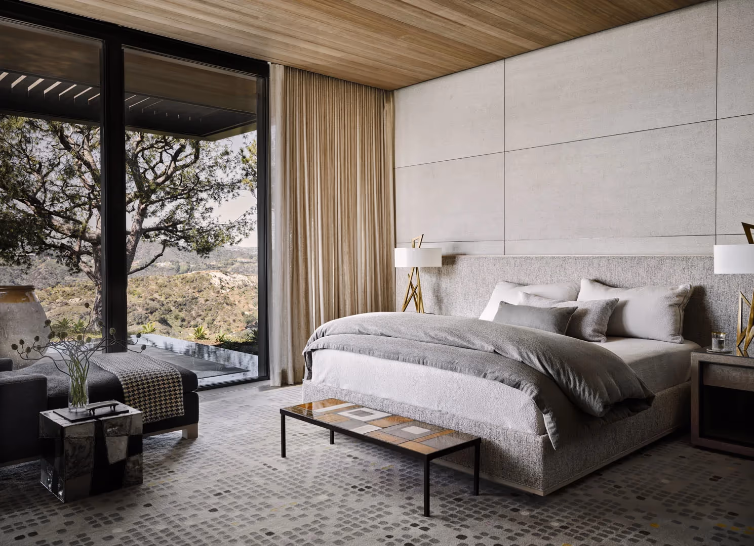 Bedroom with an upholstered bed, wood ceiling and a glass wall to an oak tree
