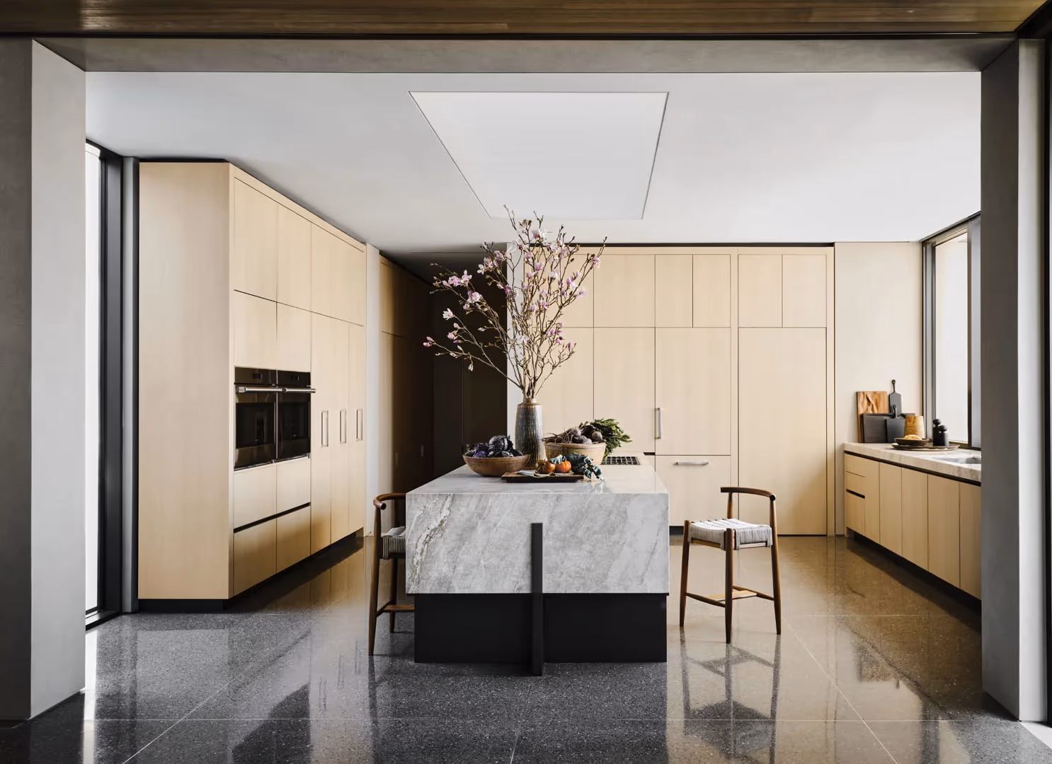 Kitchen with pale wood cabinetry, built-in ovens and a white stone island