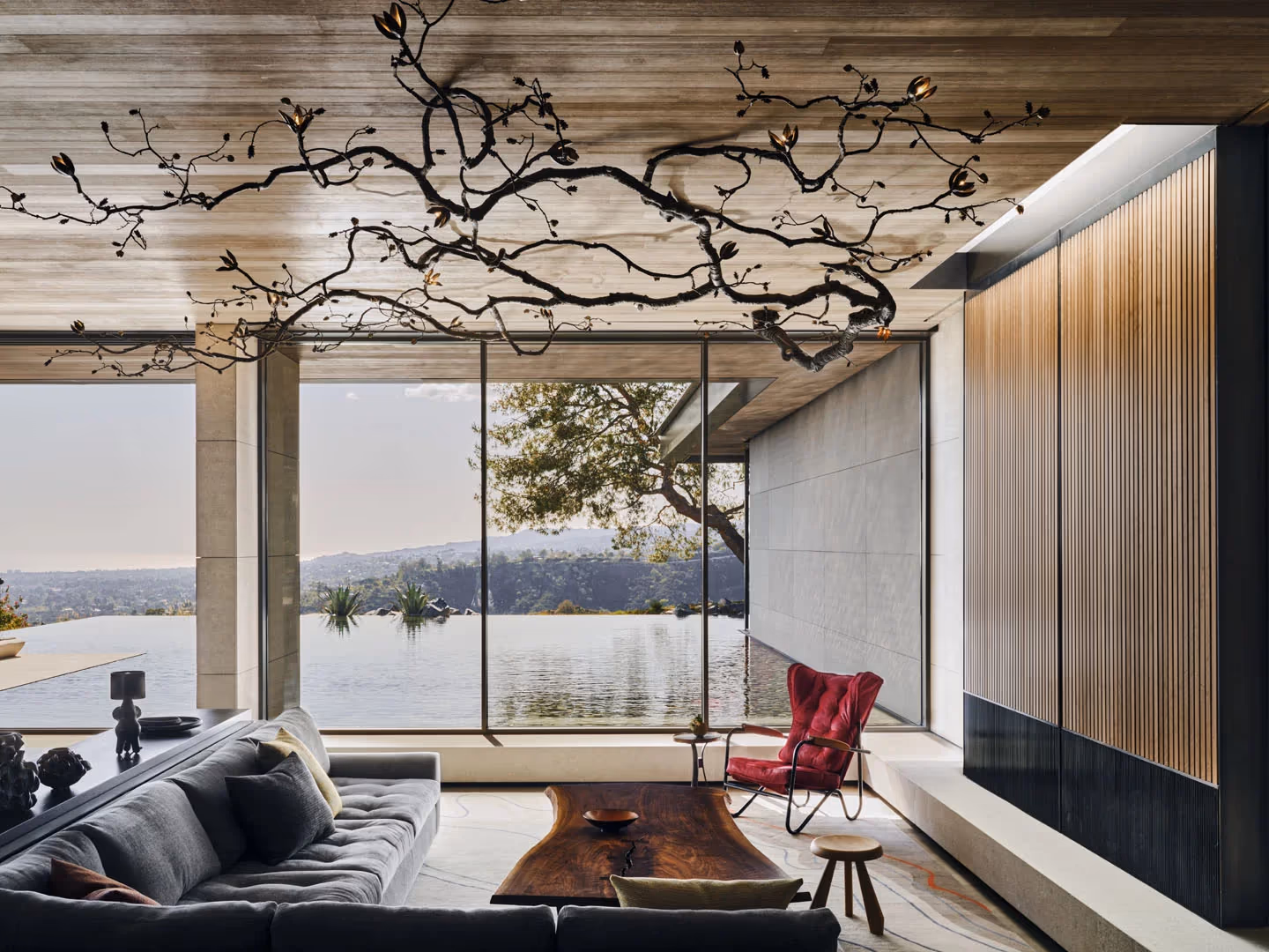 Living room with a wood ceiling, sculptural branch fixture and a full-height glass wall to the pool