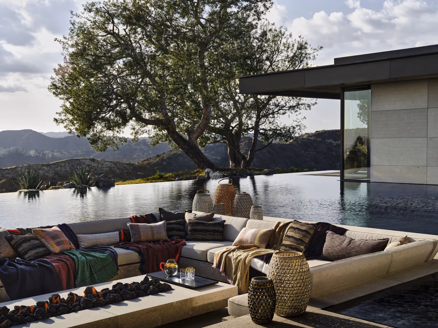 Sunken outdoor lounge with cushions set into an infinity-edge pool under an old oak