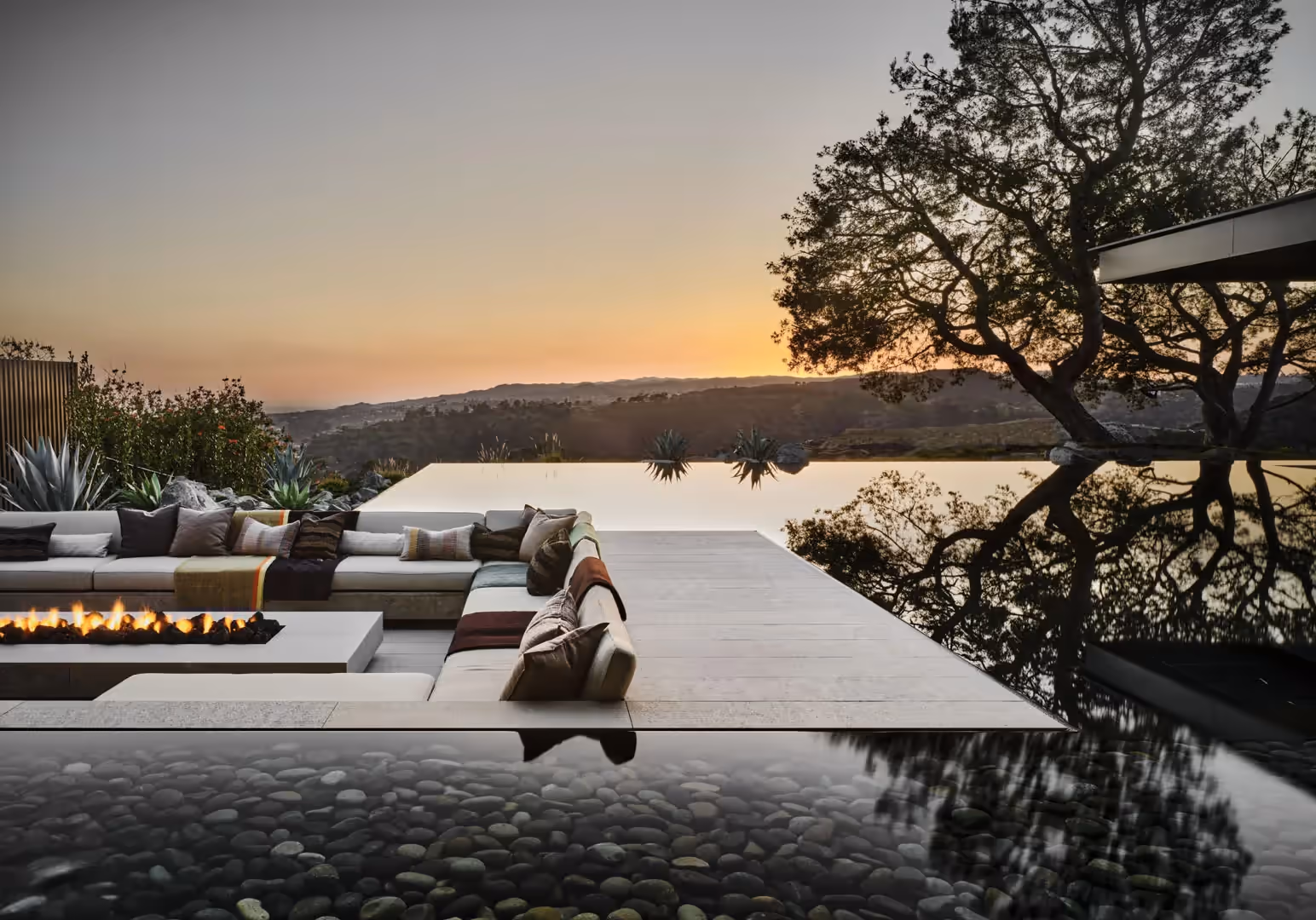 Terrace with a sunken lounge and fire feature beside a reflecting pool at sunset